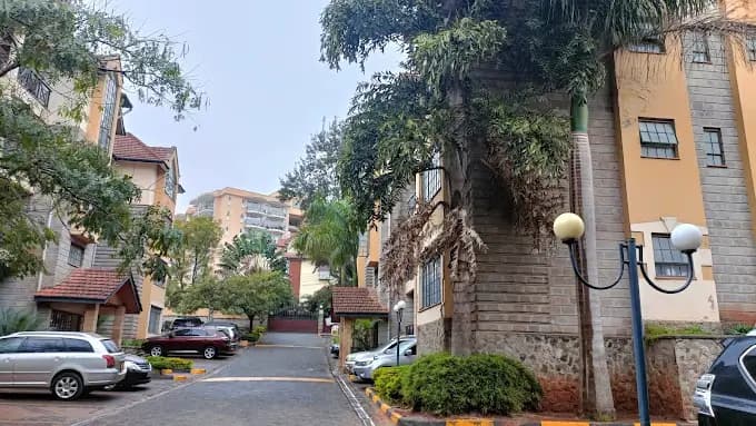 Residential compound entrance with multi-story buildings and parked cars