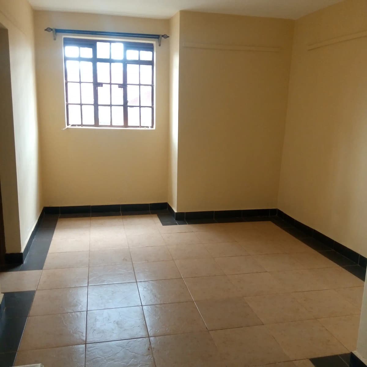 Unfurnished bedroom with barred window and tiled flooring