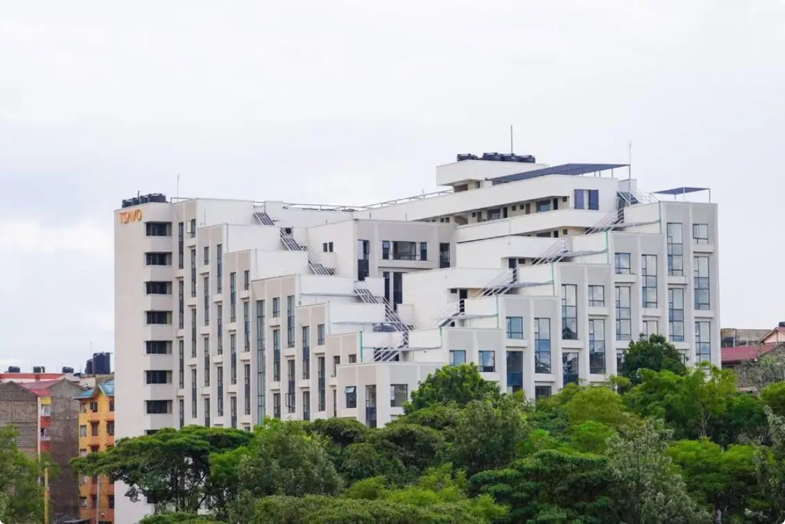 Modern multi-story apartment building with white facade and green surroundings