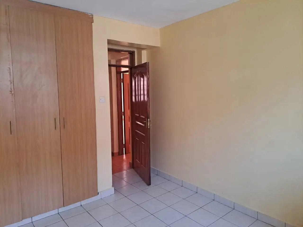 Unfurnished bedroom with wooden wardrobe and tiled floor