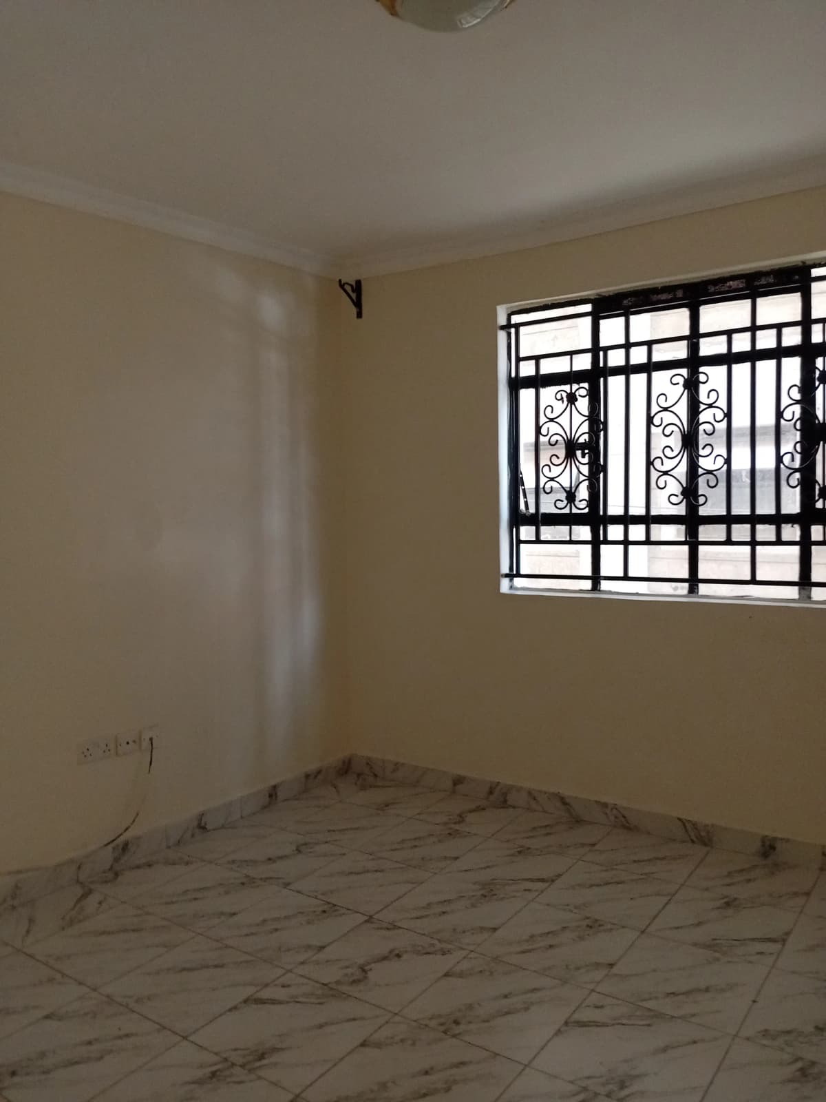 Unfurnished bedroom with barred window and tiled flooring