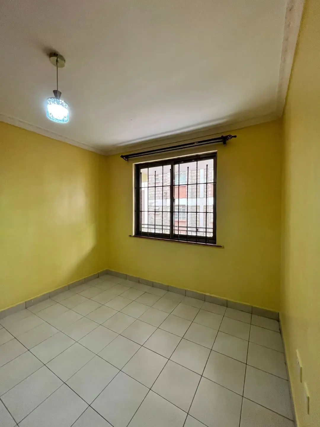 Bright yellow bedroom with barred window and tile flooring