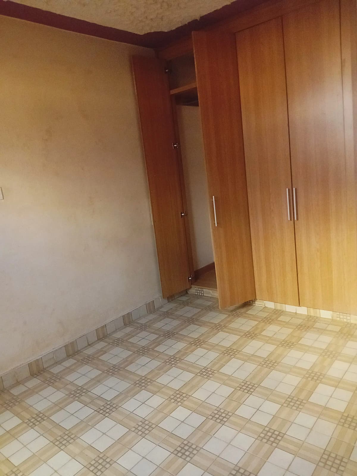 Empty bedroom with wooden wardrobe and tiled flooring