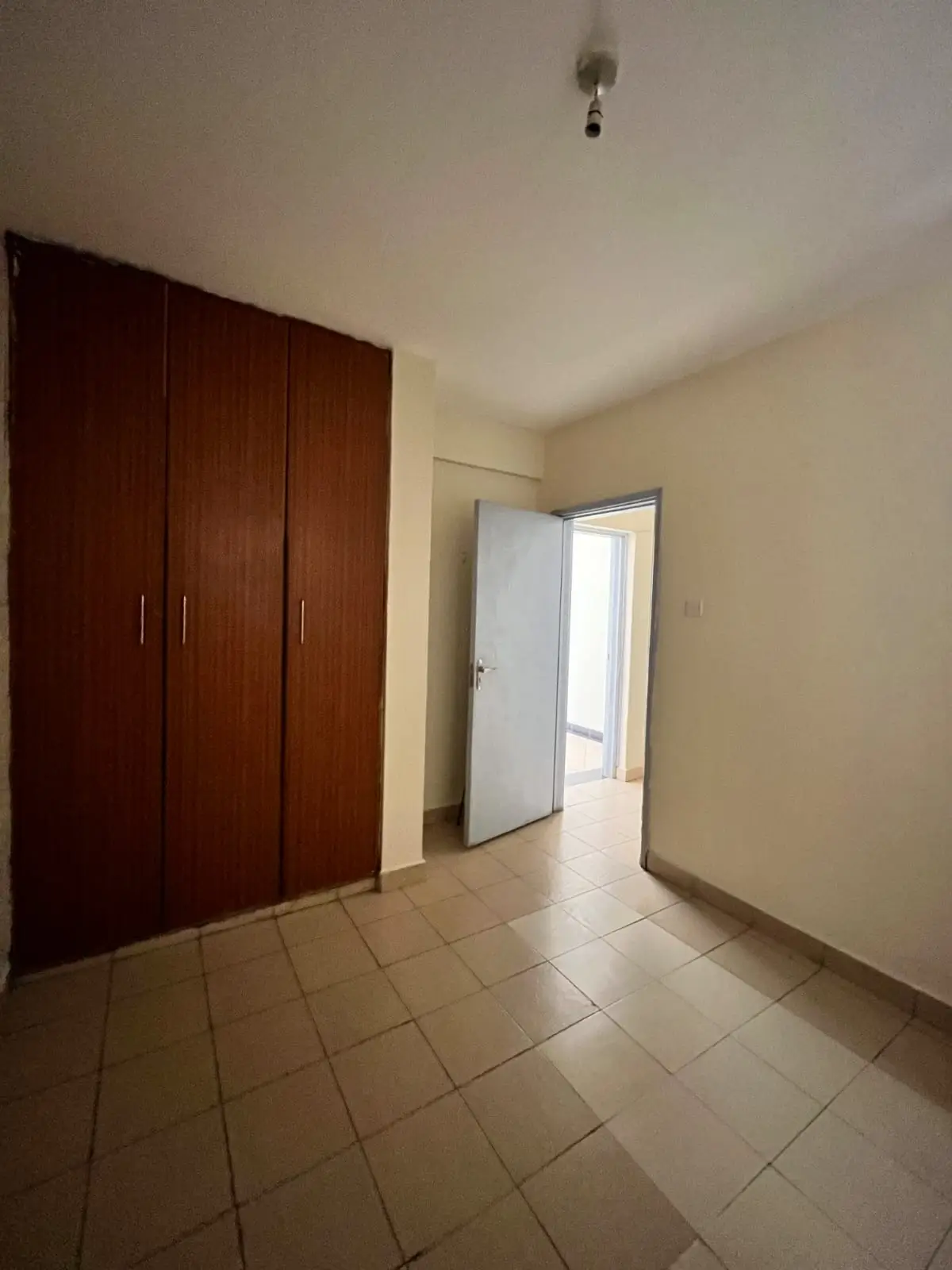 Empty bedroom with built-in wooden wardrobe and tiled flooring