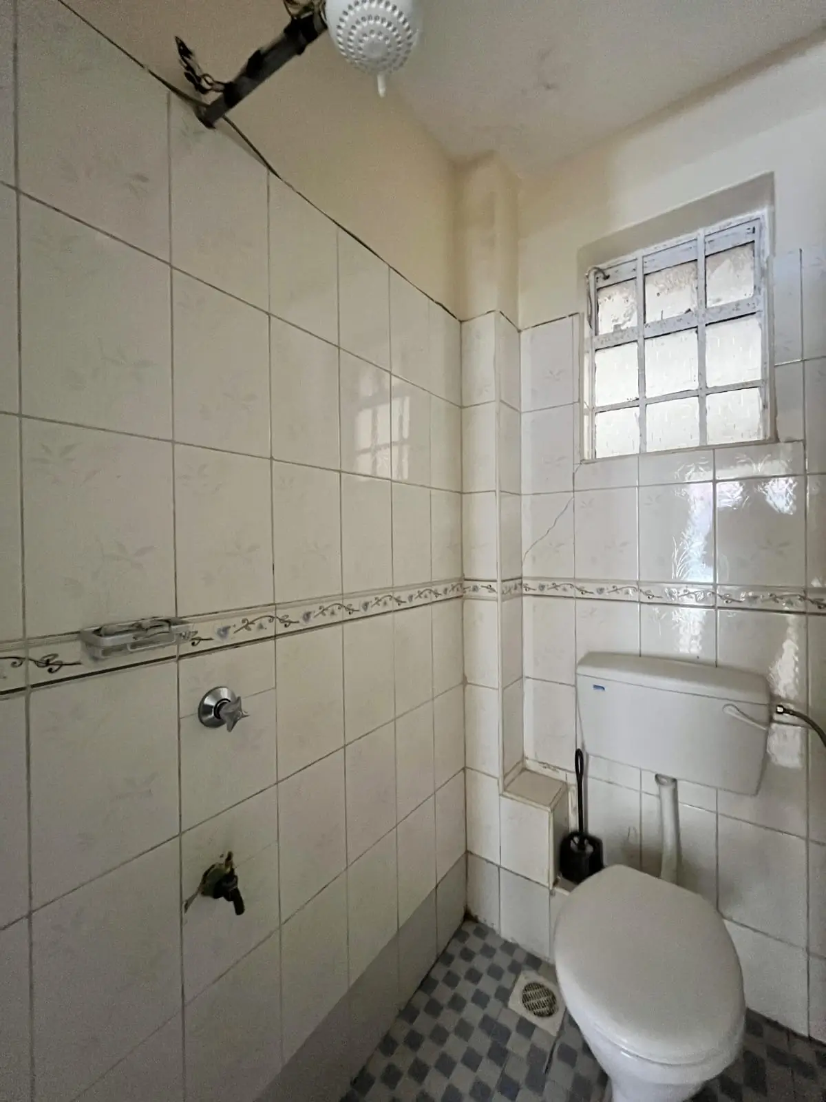 Compact bathroom with white tile walls, toilet, and shower enclosure