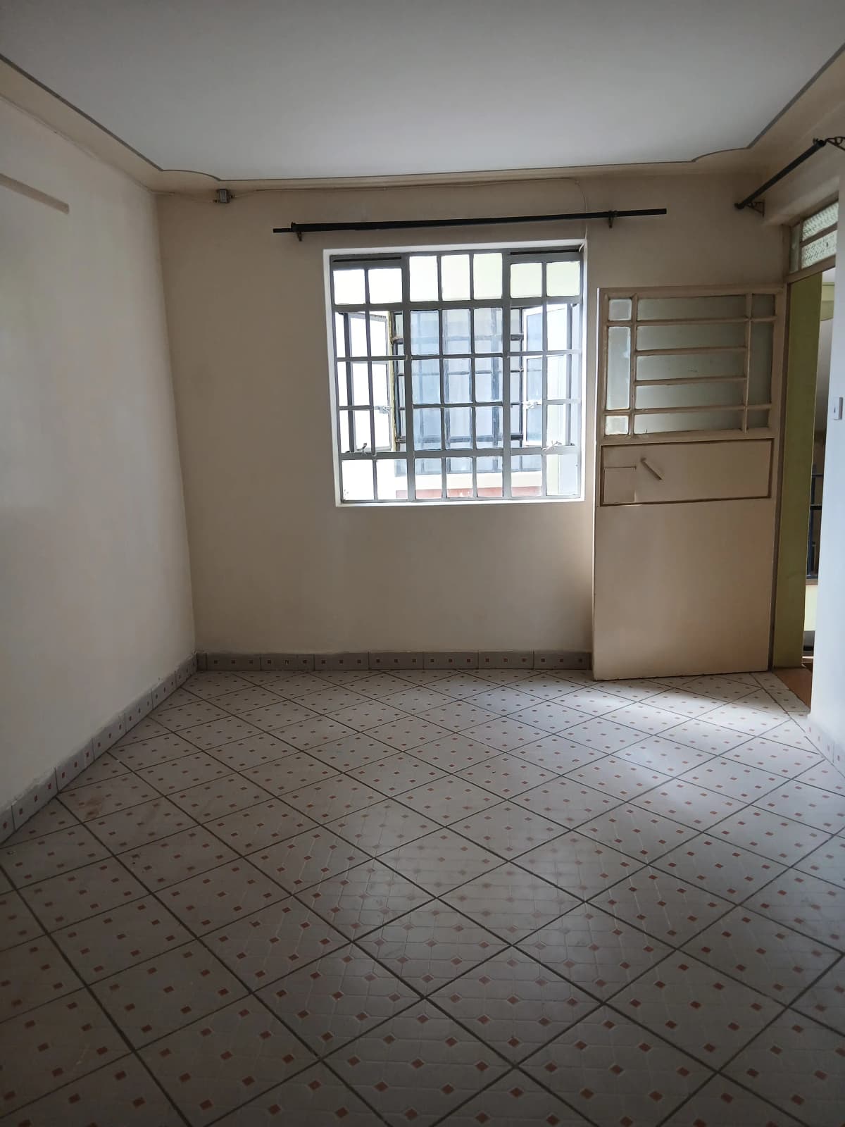 Empty living space with barred window and tiled flooring