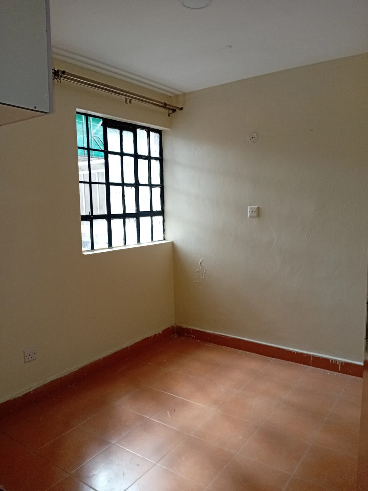 Spacious bedroom with terracotta tile flooring and barred window