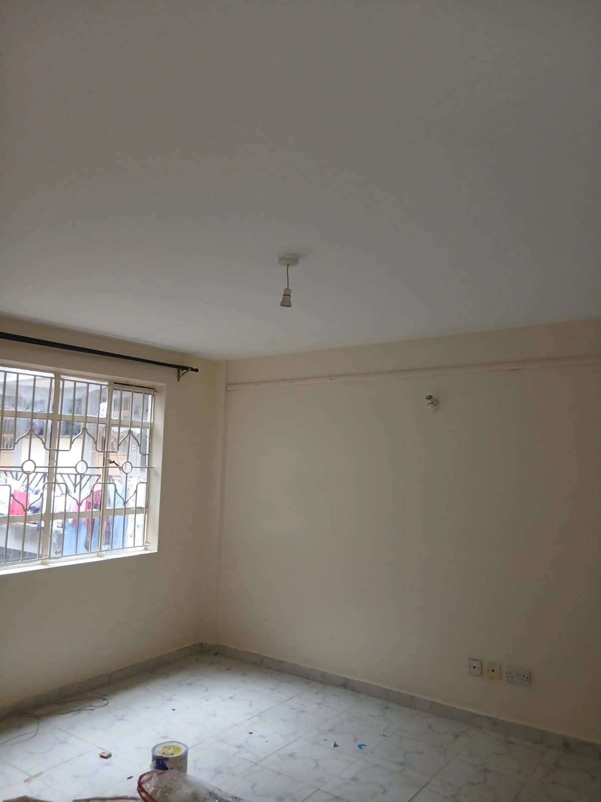 Empty bedroom with barred window and bare concrete floor