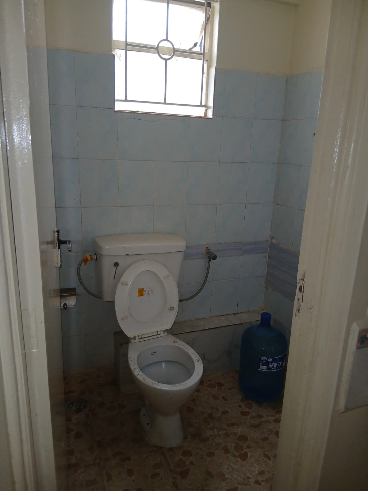 Basic toilet with window, blue tile walls, minimal fixtures