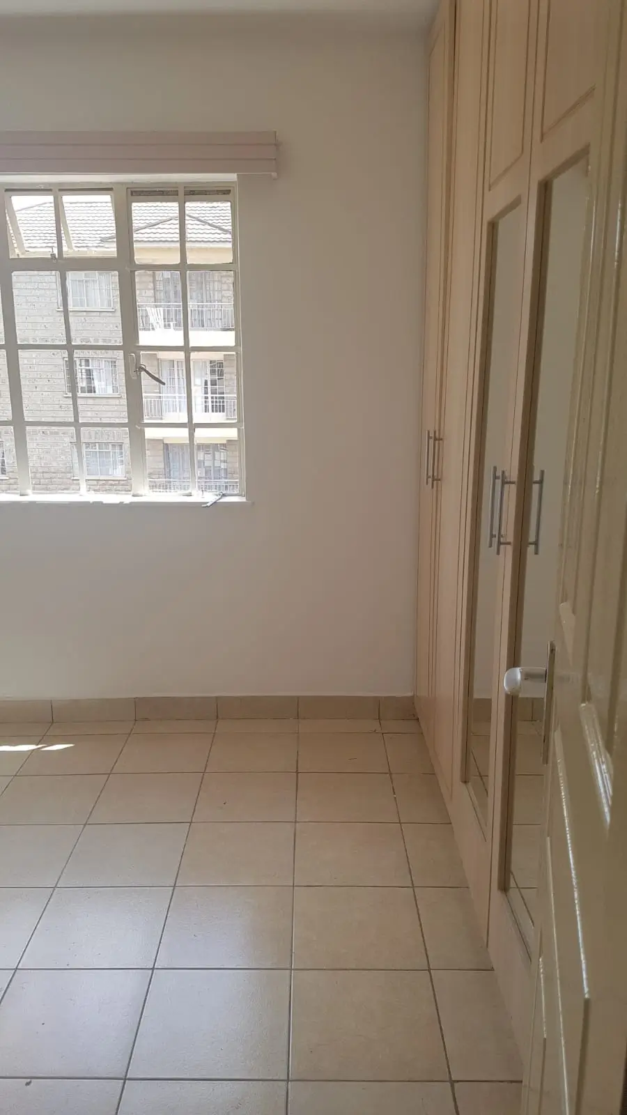 Bright empty bedroom with tiled floor and built-in wardrobes