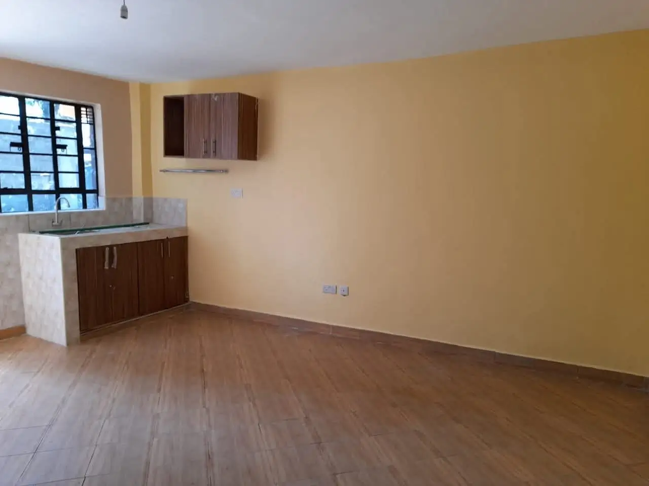 Open-plan living room with kitchenette, wooden flooring, yellow walls