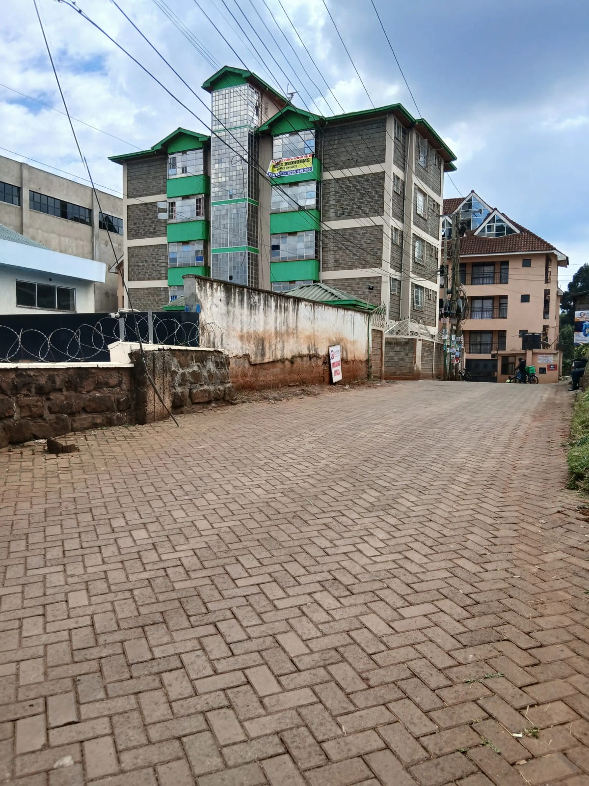 Multi-story residential building with green window frames, paved compound