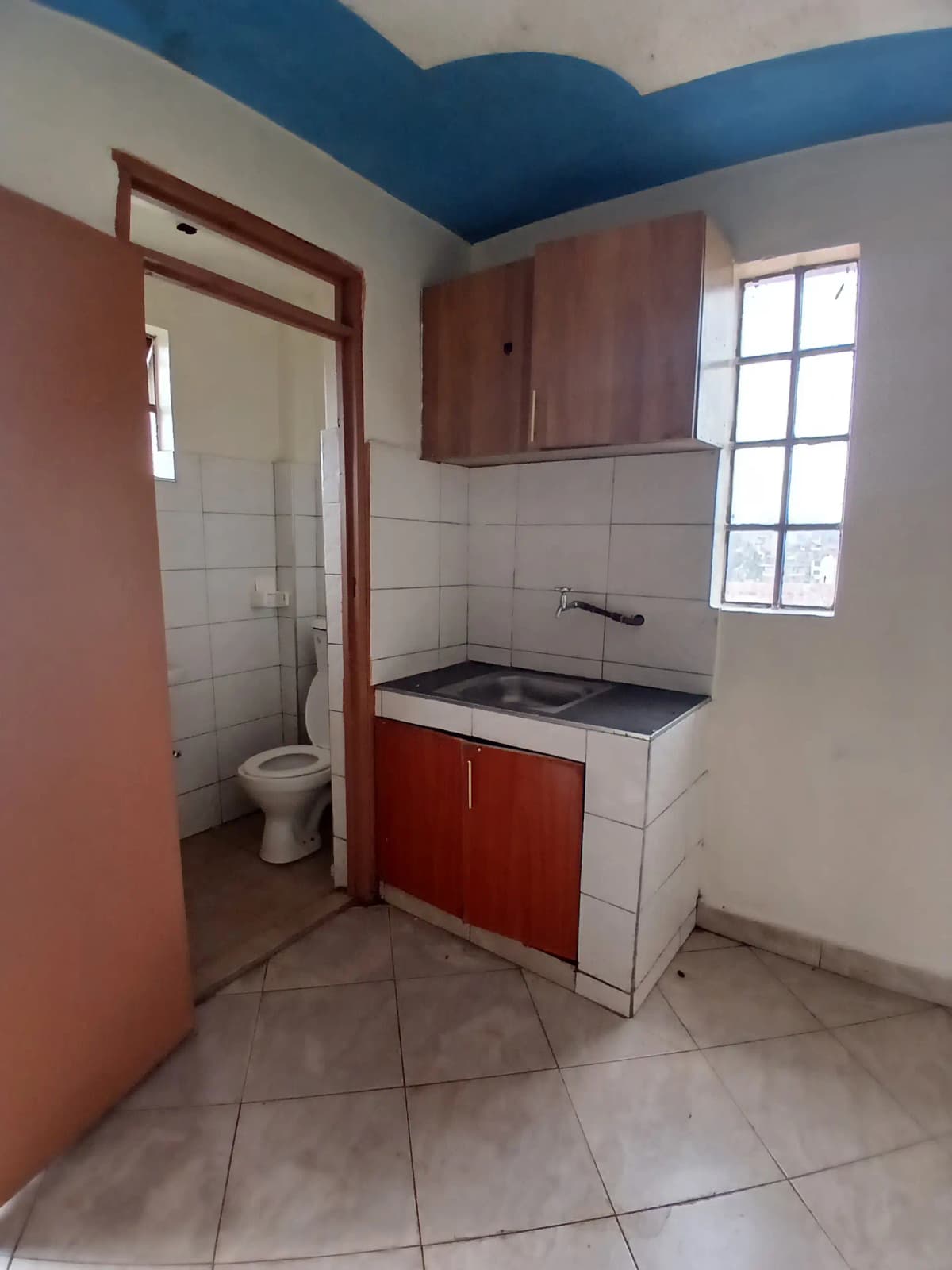Compact kitchen with red cabinet and stove, toilet visible through doorway