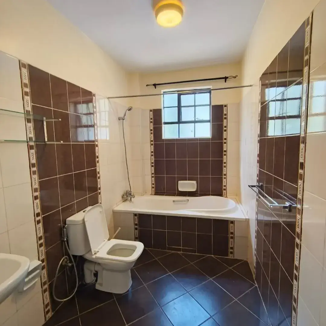 Spacious bathroom with brown tile walls, bathtub, and toilet