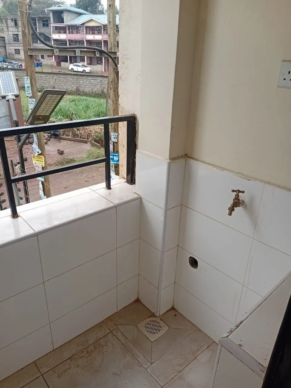 Small bathroom with tiled walls, window overlooking compound area