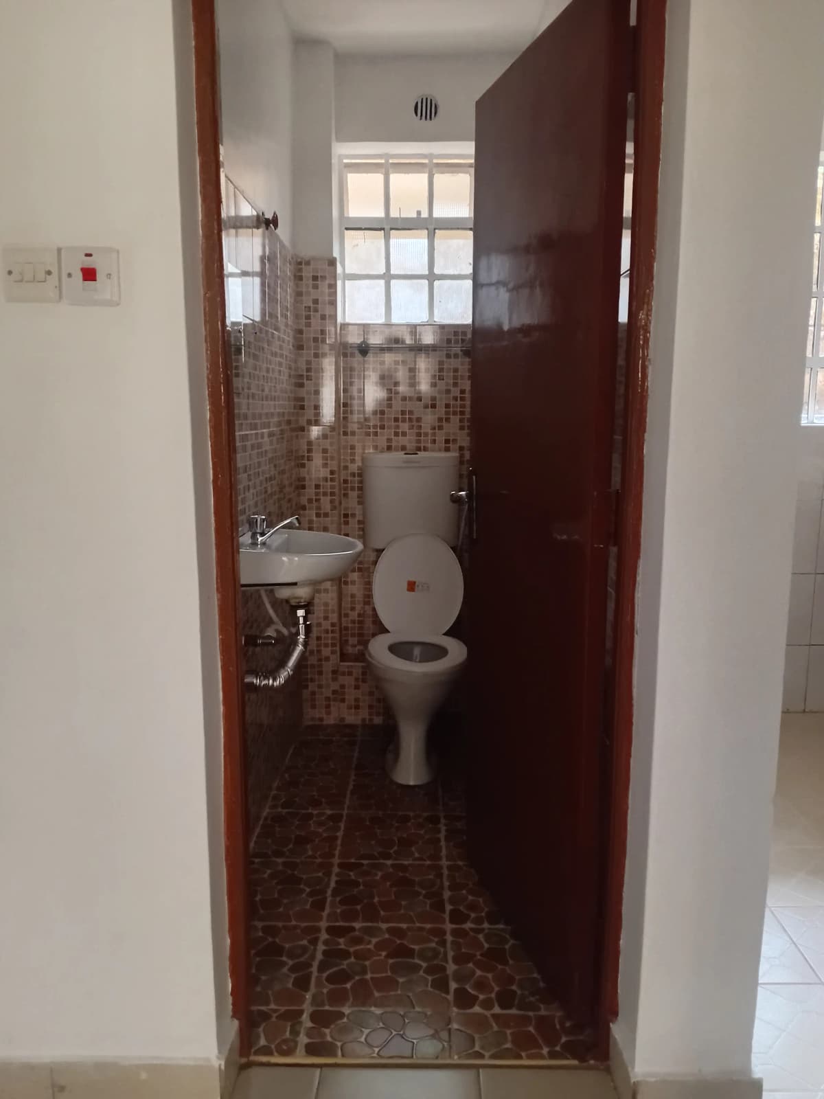 Compact bathroom with toilet, sink, brown tile flooring