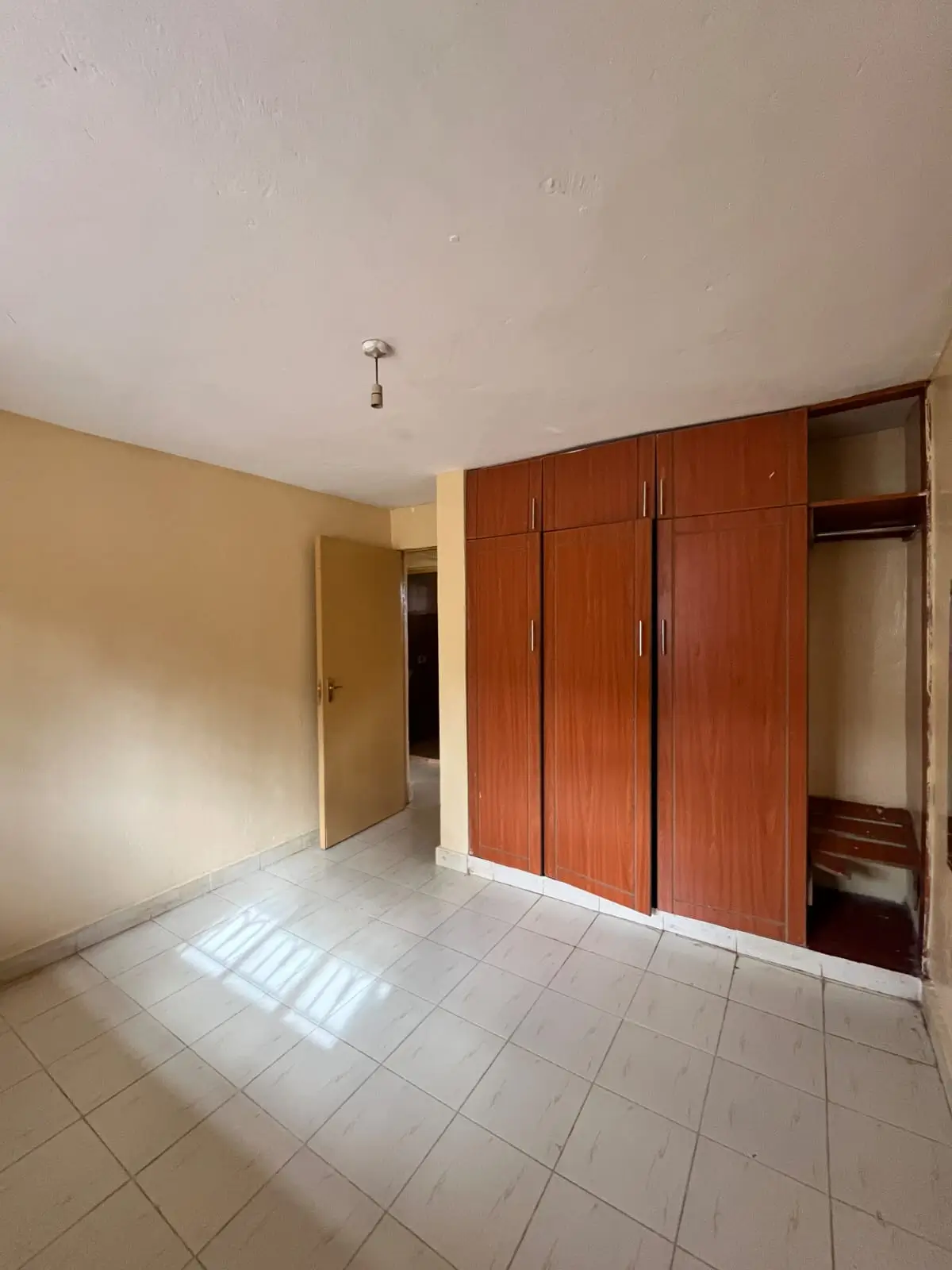 Spacious bedroom with wooden wardrobe and tiled flooring