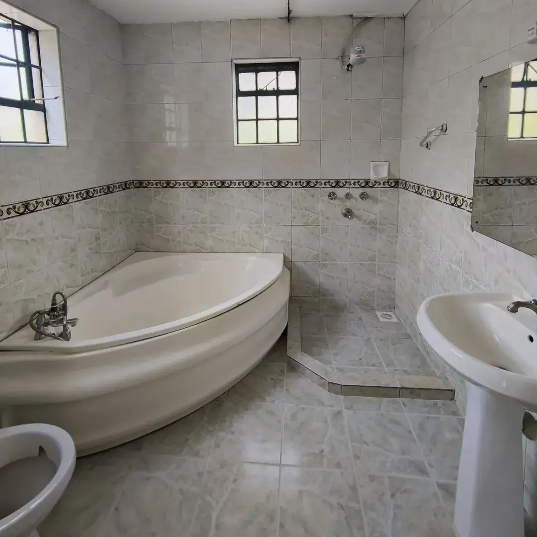 Spacious bathroom with corner bathtub, pedestal sink, toilet