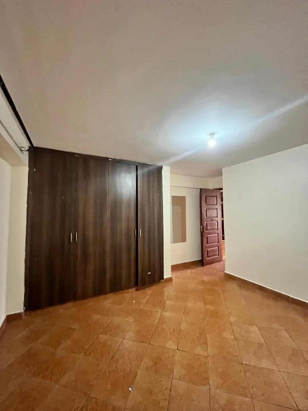 Spacious bedroom with wooden wardrobe and terracotta flooring