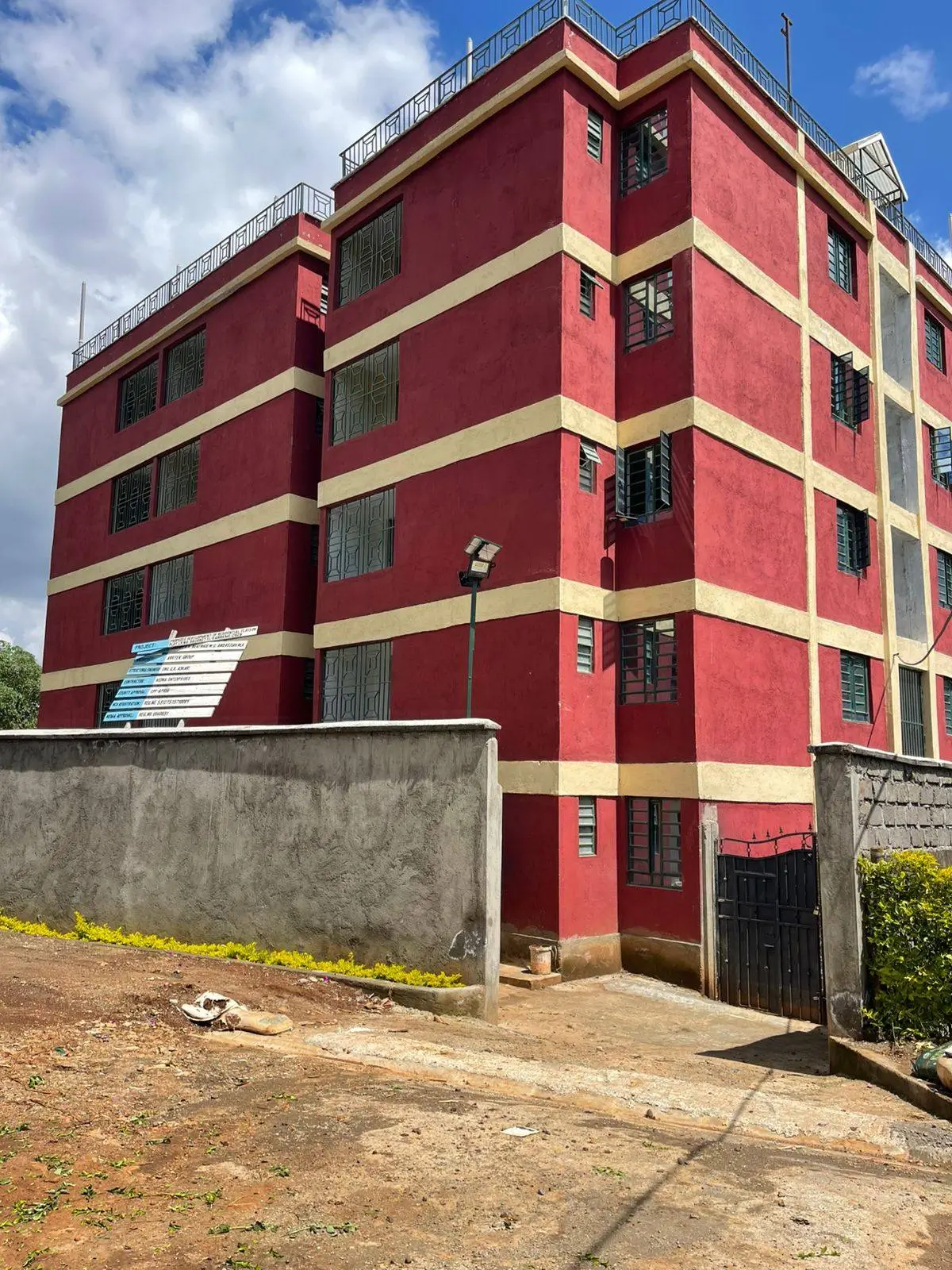 Red multi-story residential building with compound entrance gate