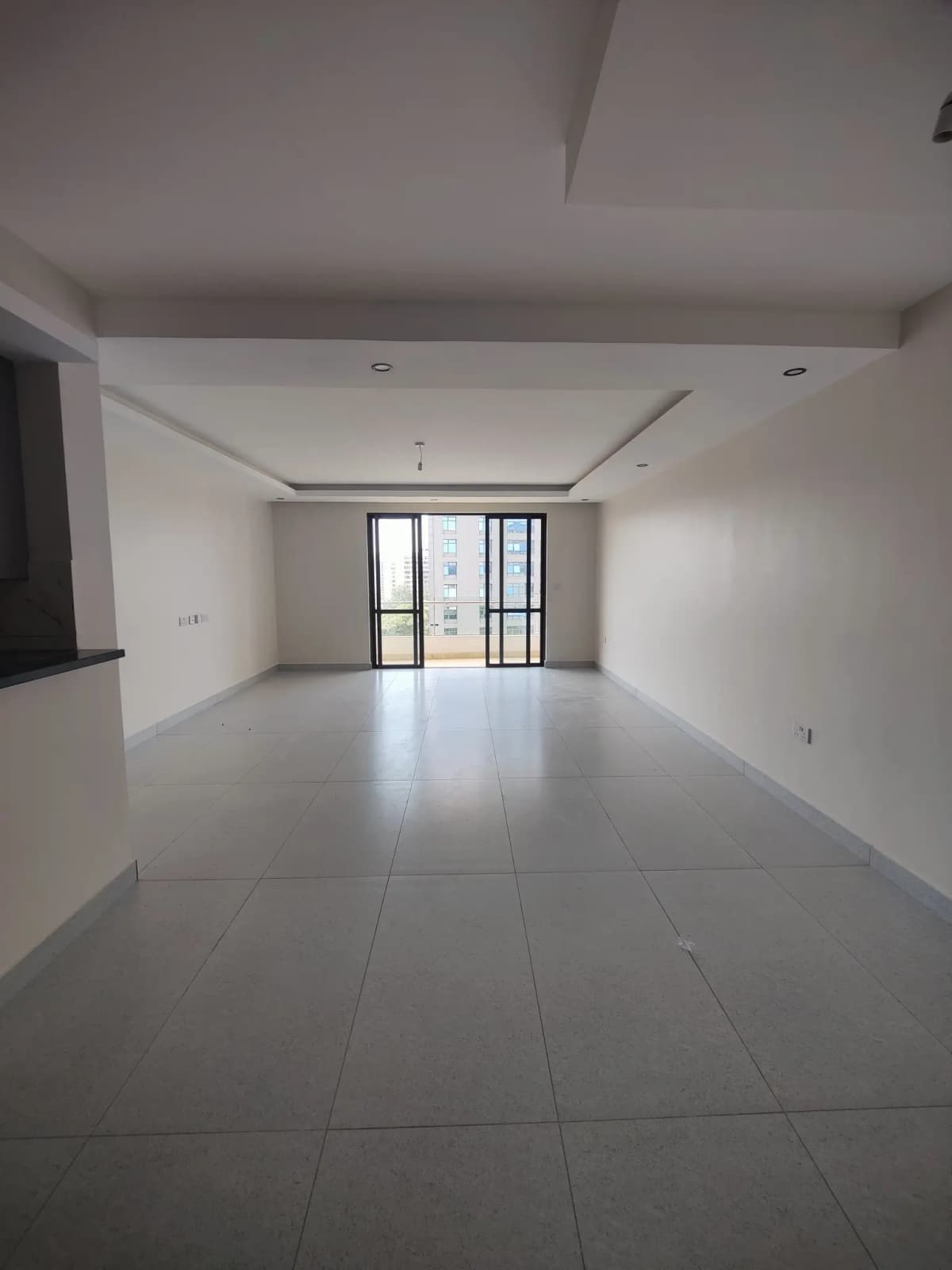 Spacious empty living room with tiled flooring and glass balcony doors