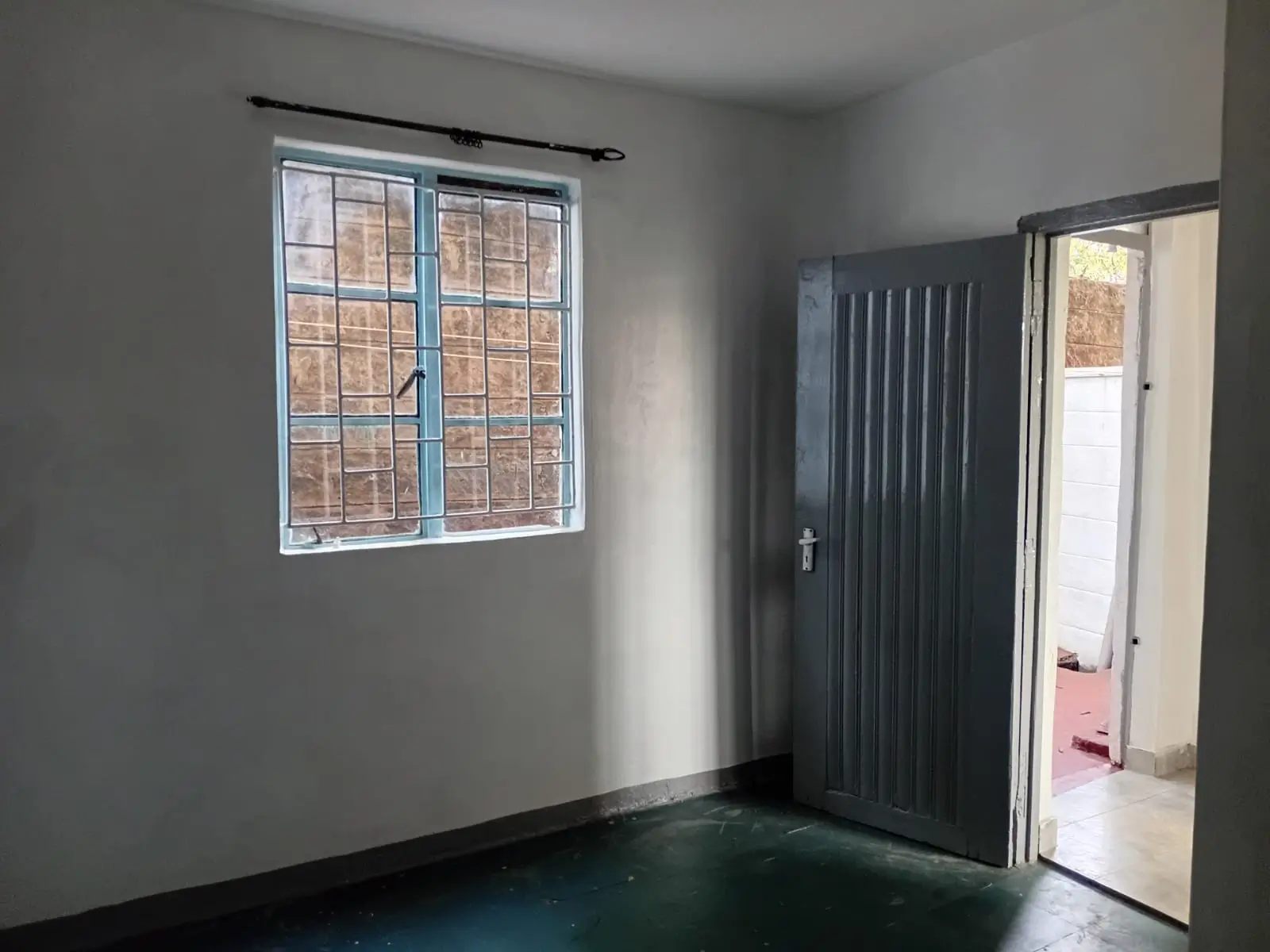 Sparse bedroom with barred window and dark green flooring