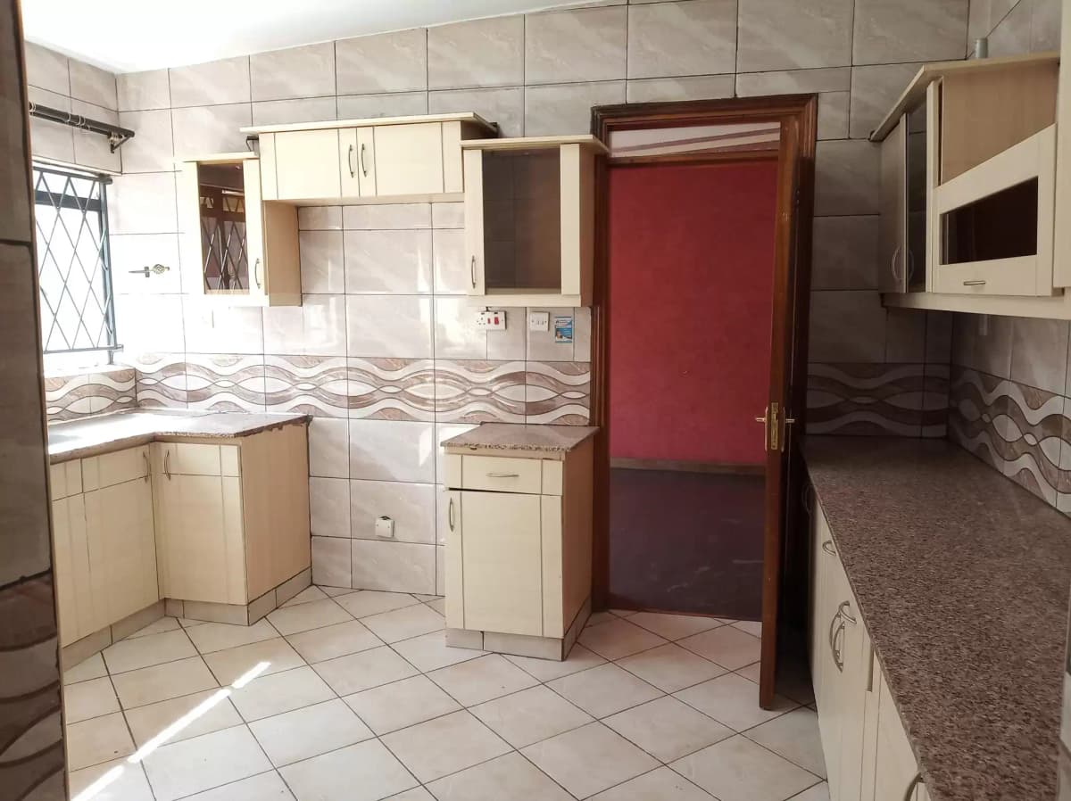 Spacious kitchen with tiled counters, cream cabinets, red door