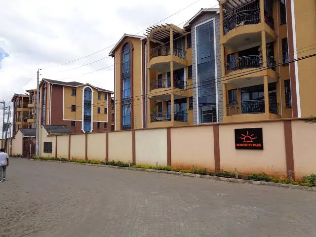 Multi-story residential building with yellow facade and perimeter wall