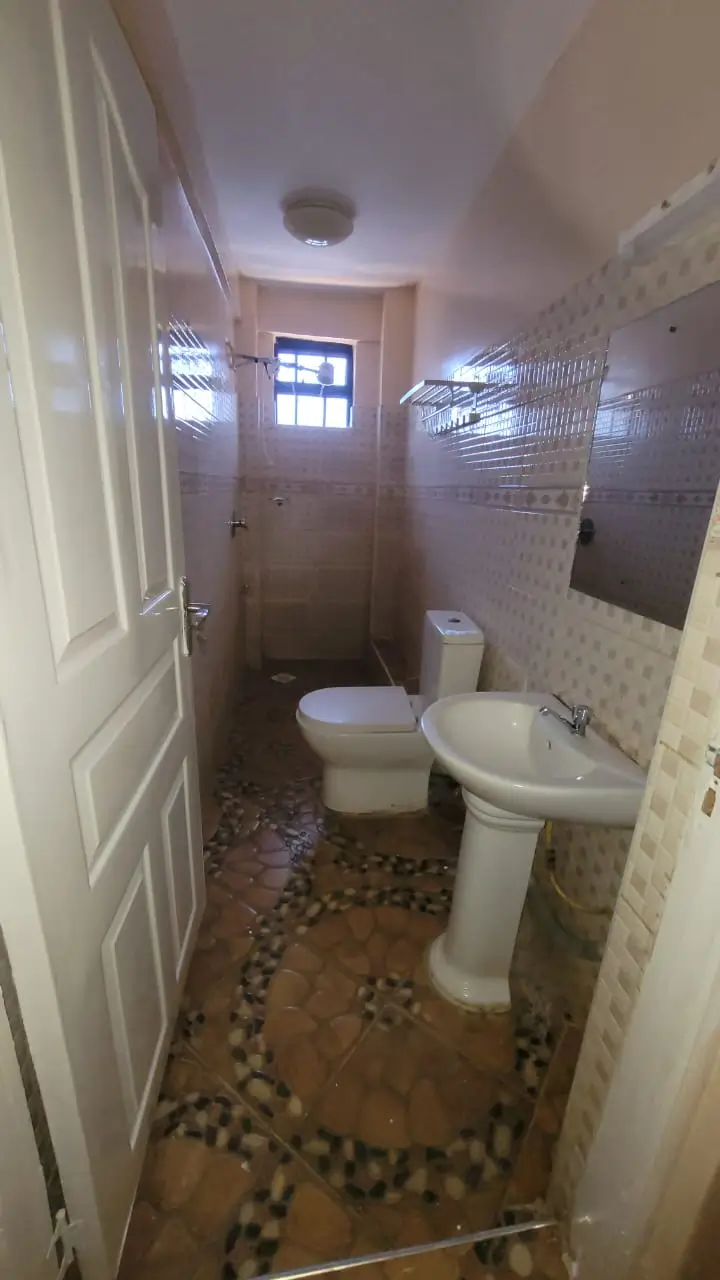 Compact bathroom with toilet, pedestal sink, and tiled walls