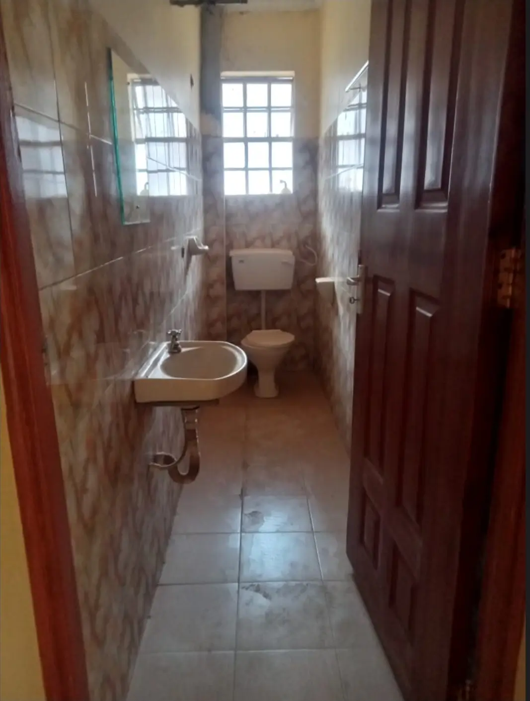 Narrow bathroom with pedestal sink, toilet, and tiled walls