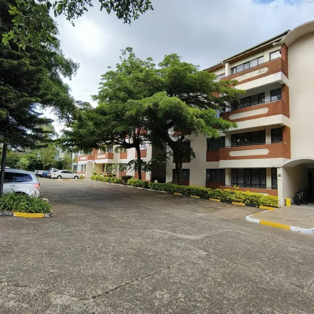 Multi-story residential building with mature trees and parking area