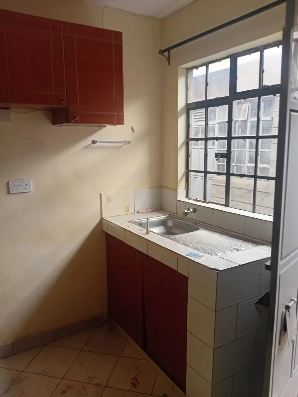Compact kitchen with red cabinetry and window overlooking street
