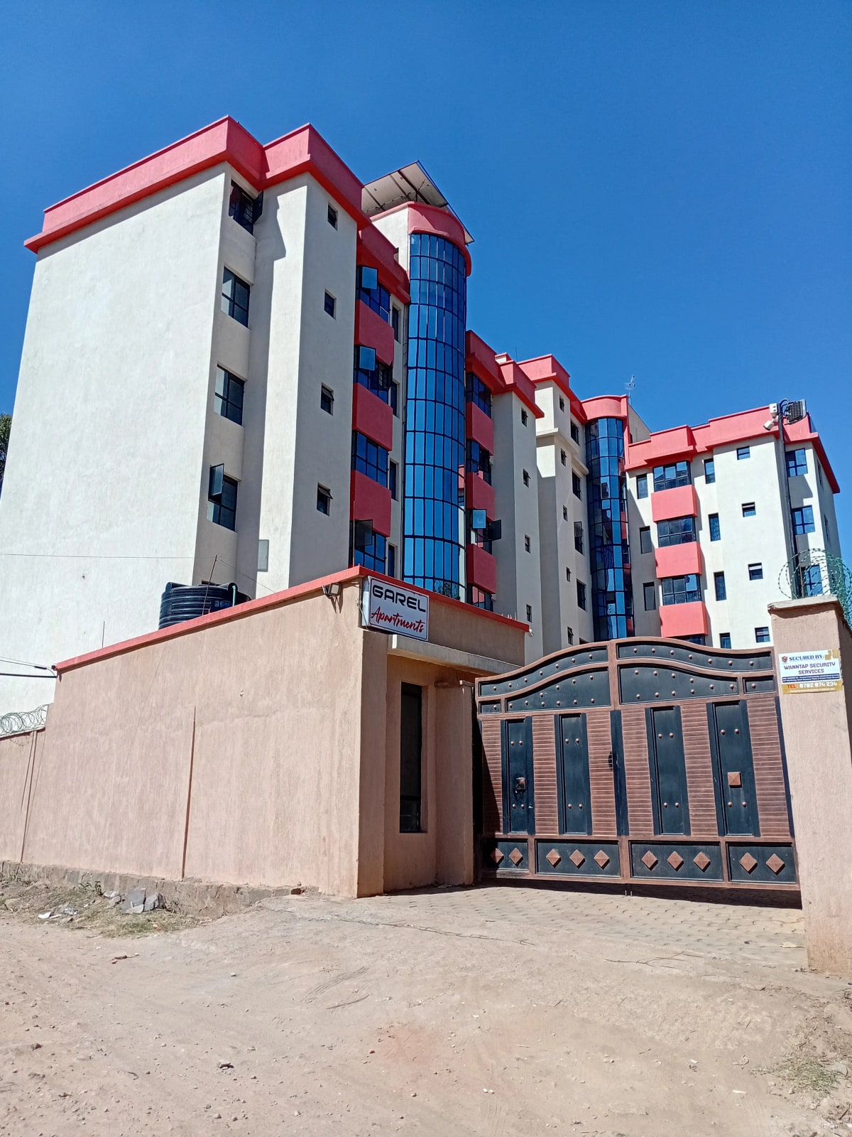 Modern apartment building with red roof and blue accents, compound gate