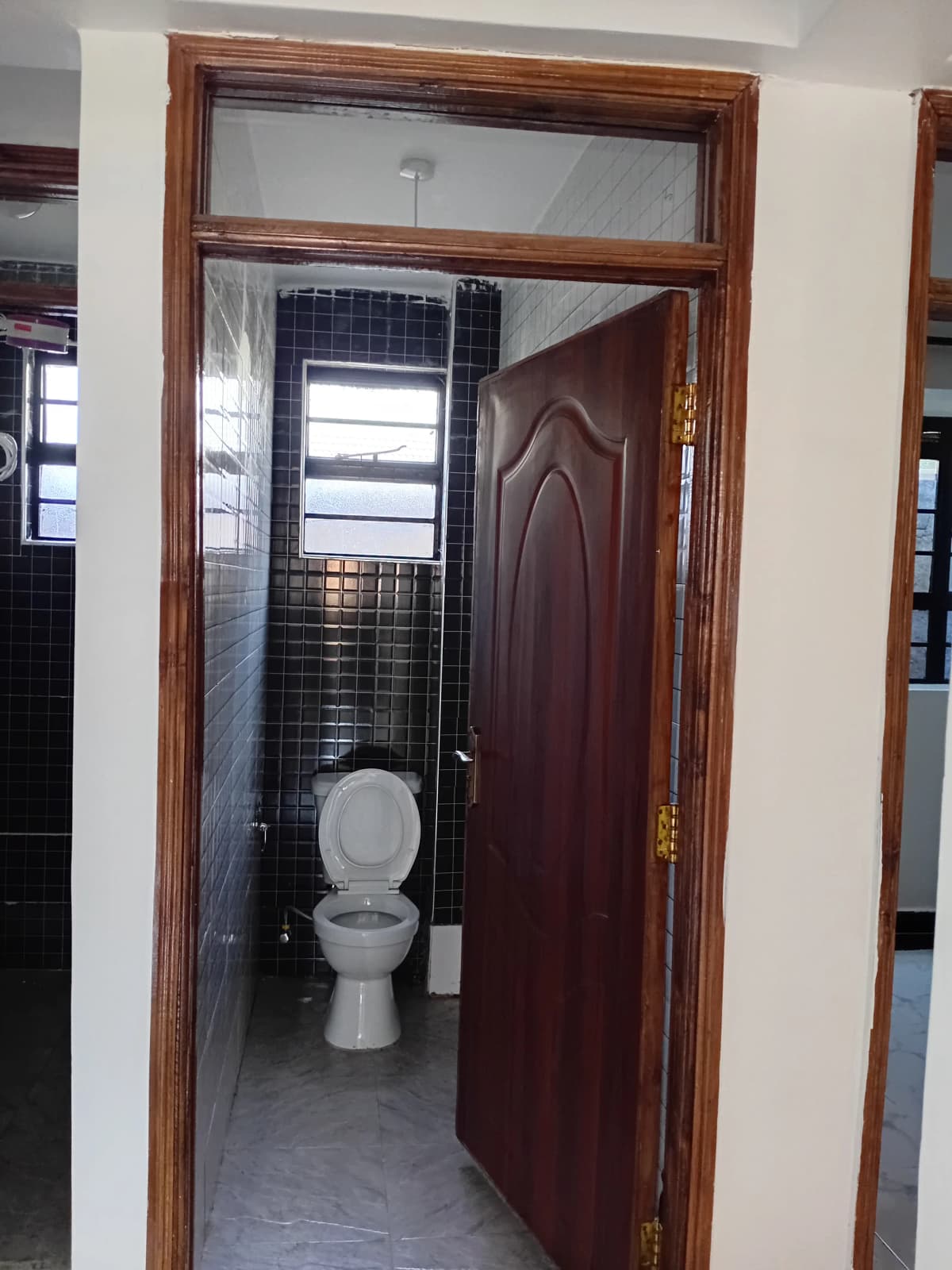 Compact bathroom with toilet, dark tile walls, small window