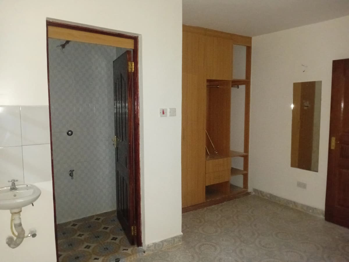 Unfurnished bedroom with open bathroom entrance and wooden shelving
