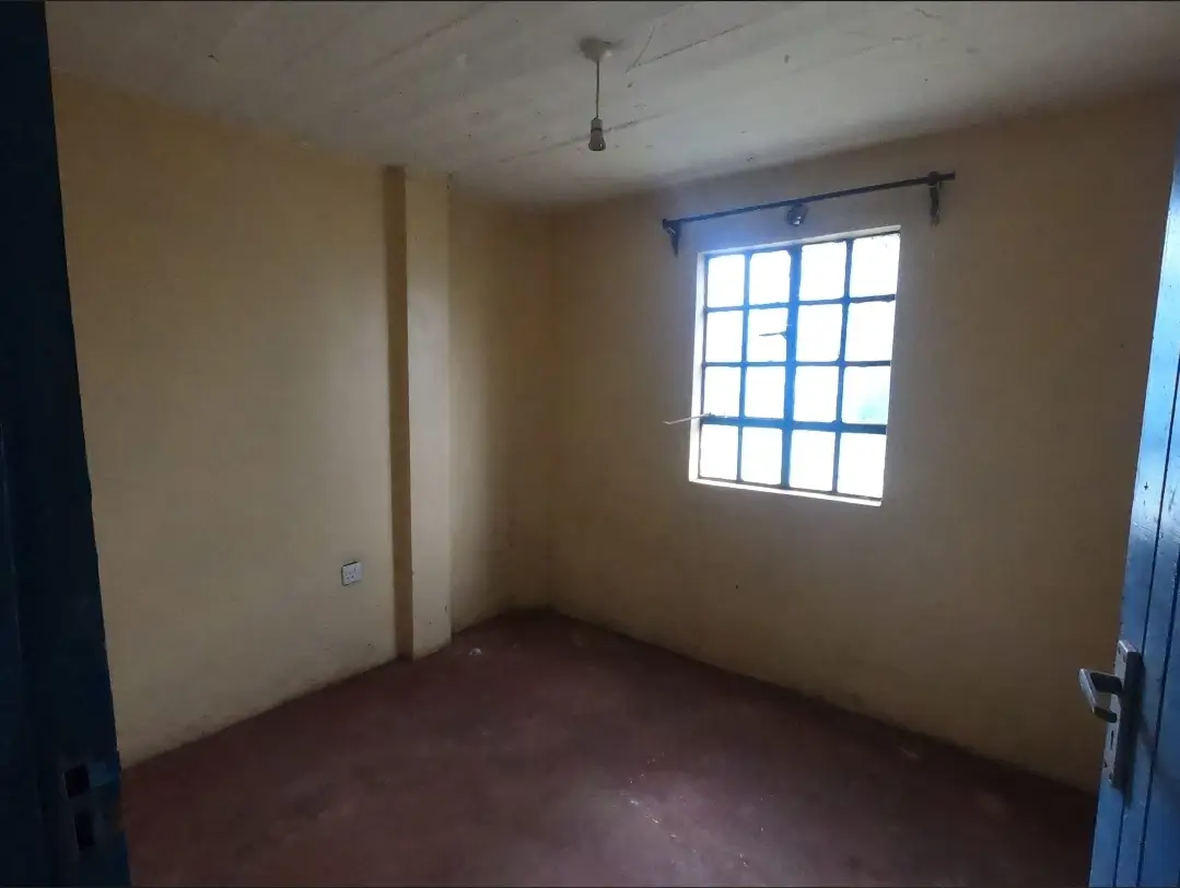 Empty bedroom with barred window and reddish floor