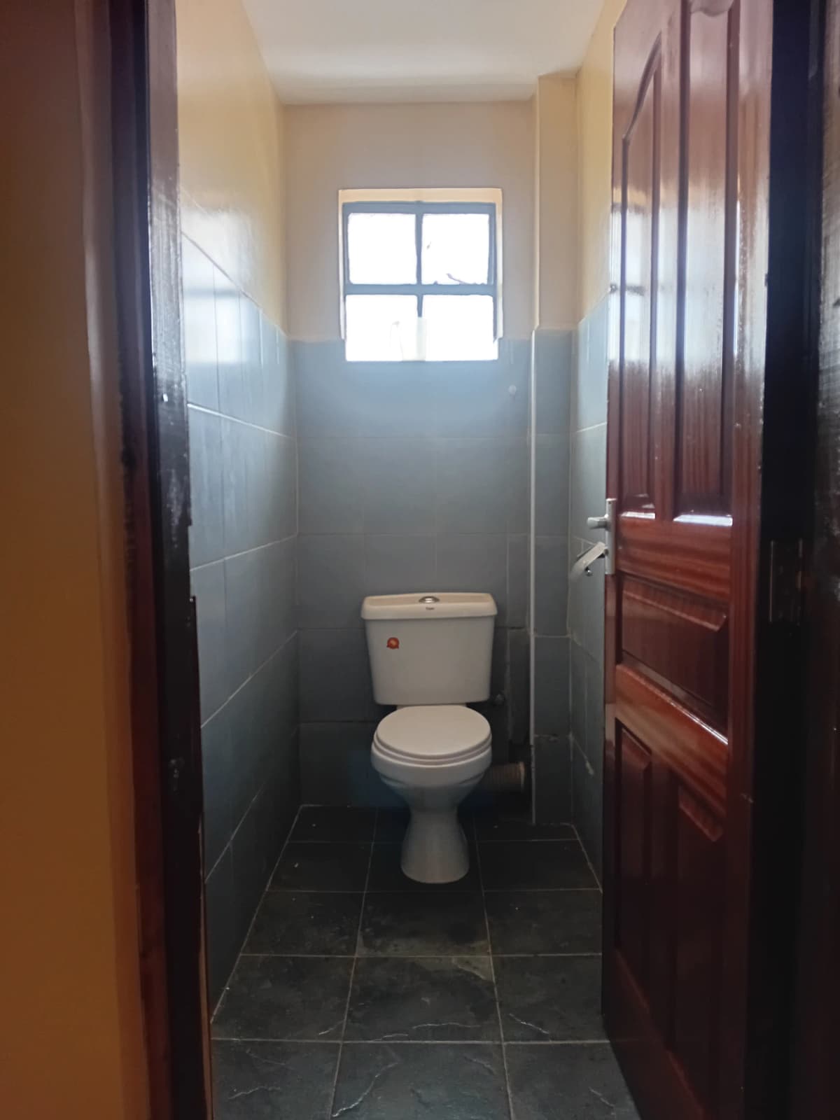 Compact bathroom with toilet, window, and dark tile flooring