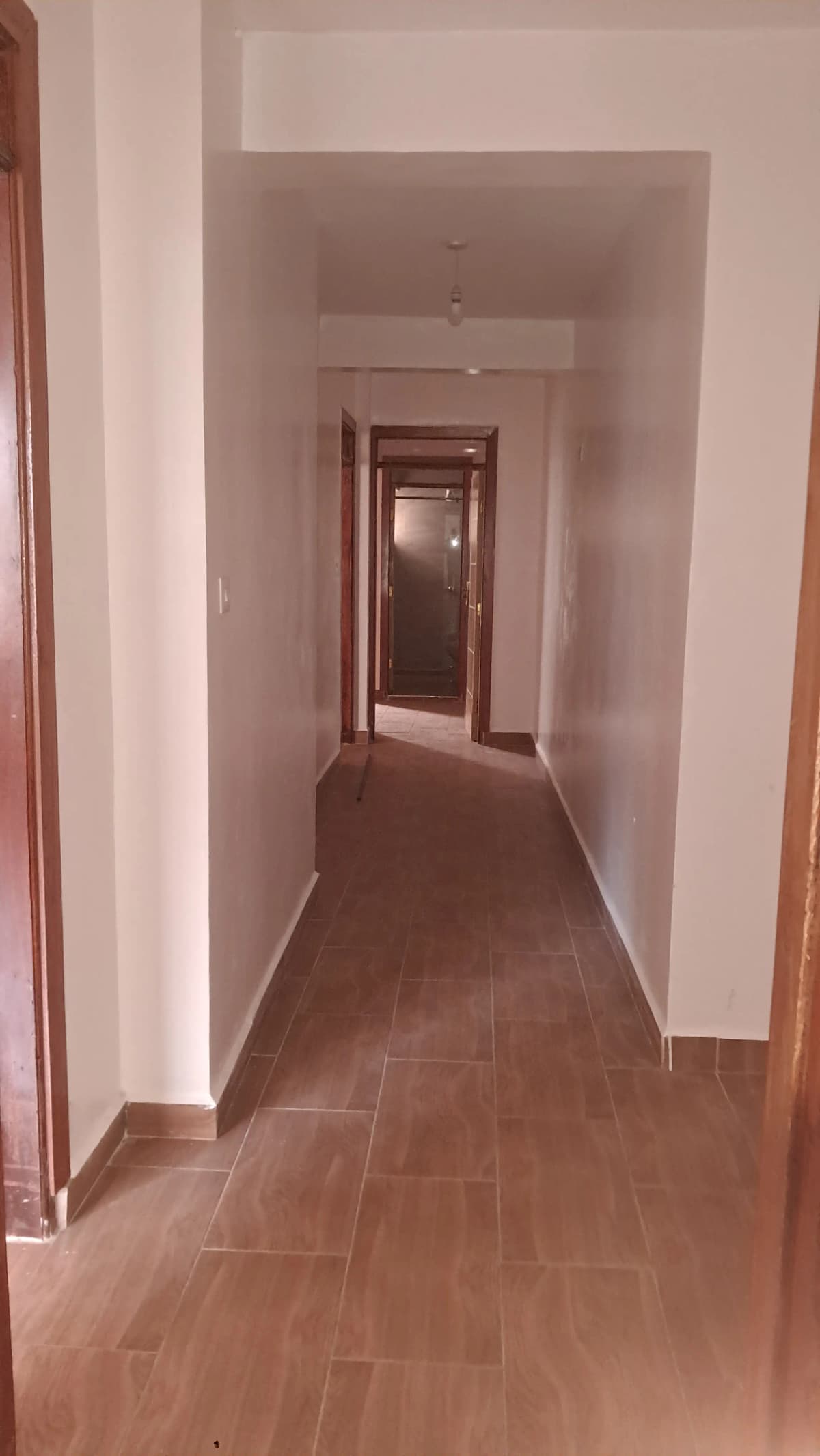 Long hallway with terracotta tile flooring and white walls