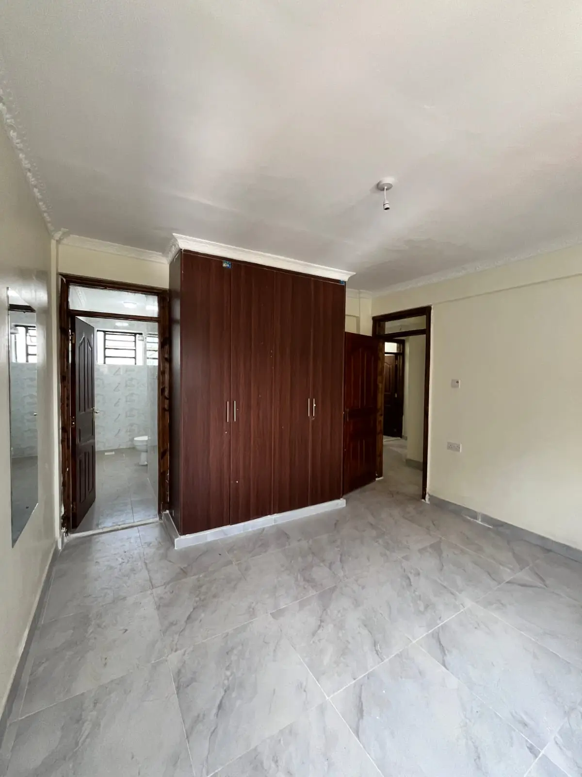 Spacious bedroom with dark wood wardrobe and marble flooring