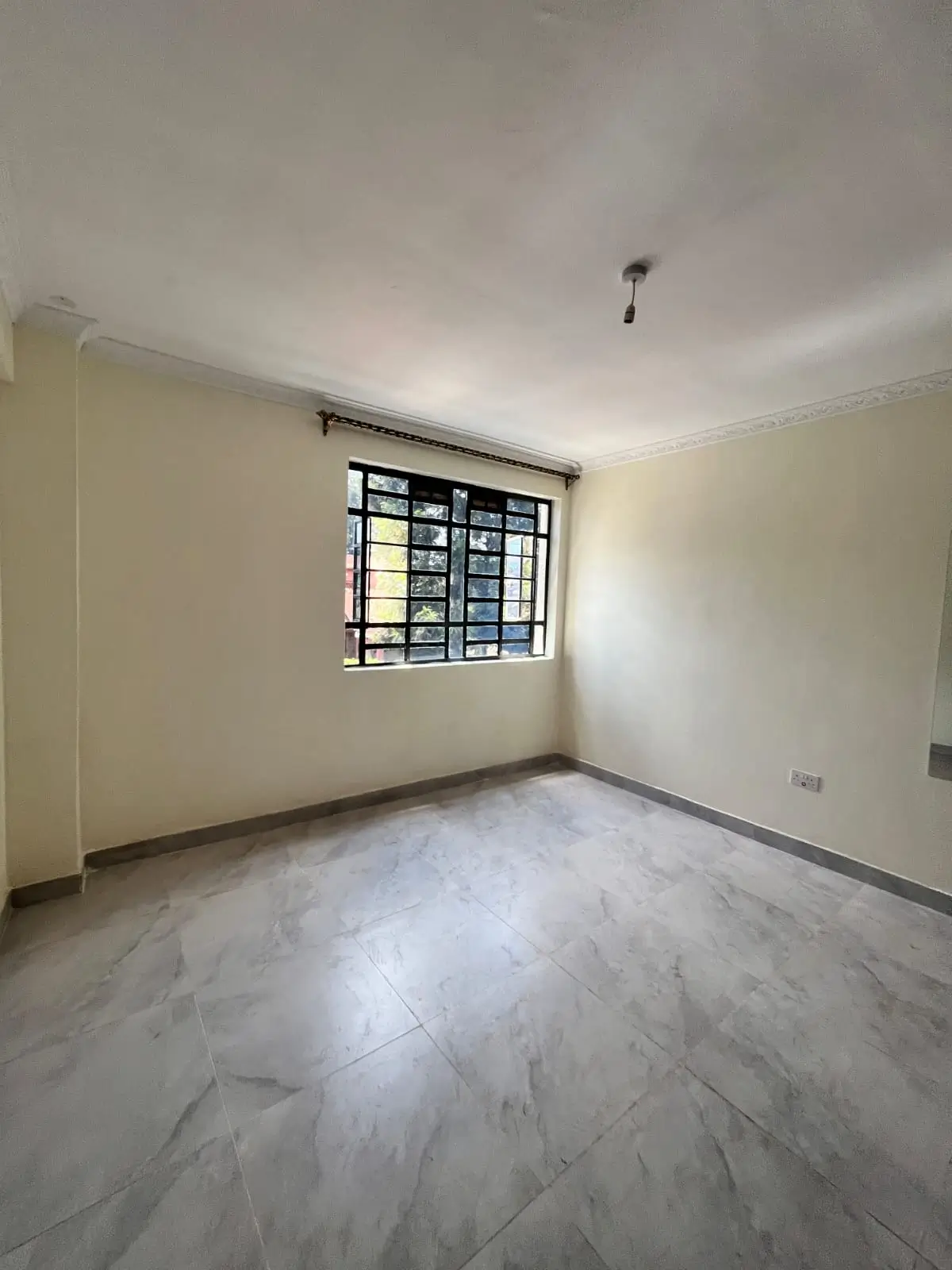 Spacious bedroom with marble flooring and barred window