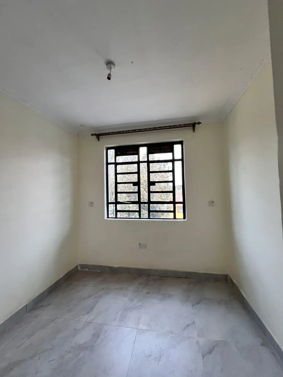 Unfurnished bedroom with barred window and bare concrete floor