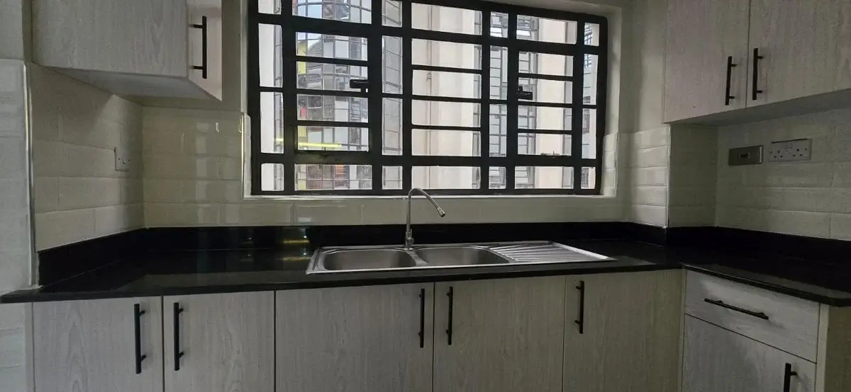 Modern kitchen with black countertop, white cabinetry, grid window