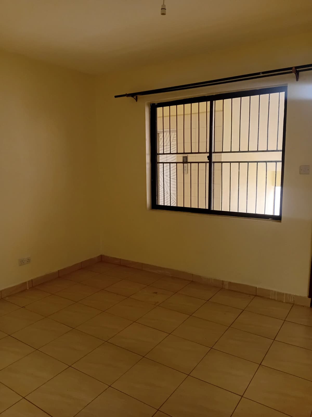 Empty bedroom with barred window and tiled flooring