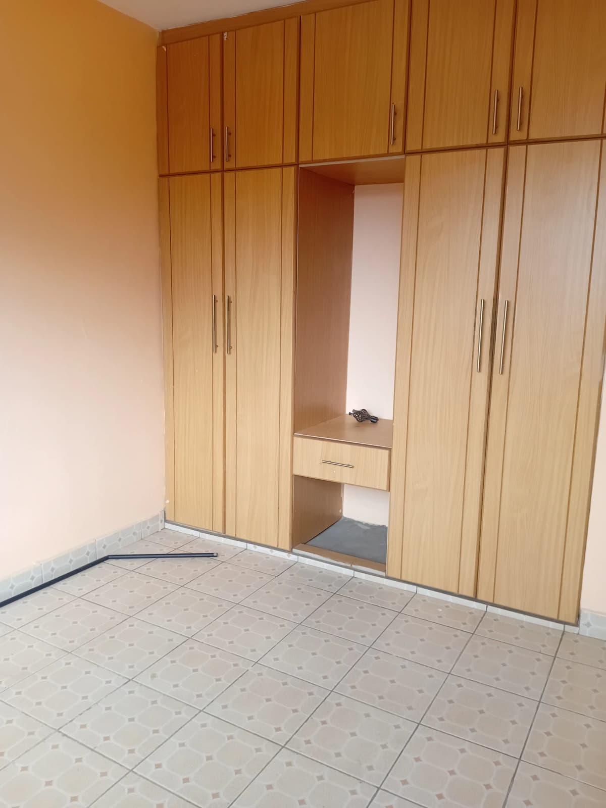 Empty bedroom with built-in wooden wardrobe and tiled floor