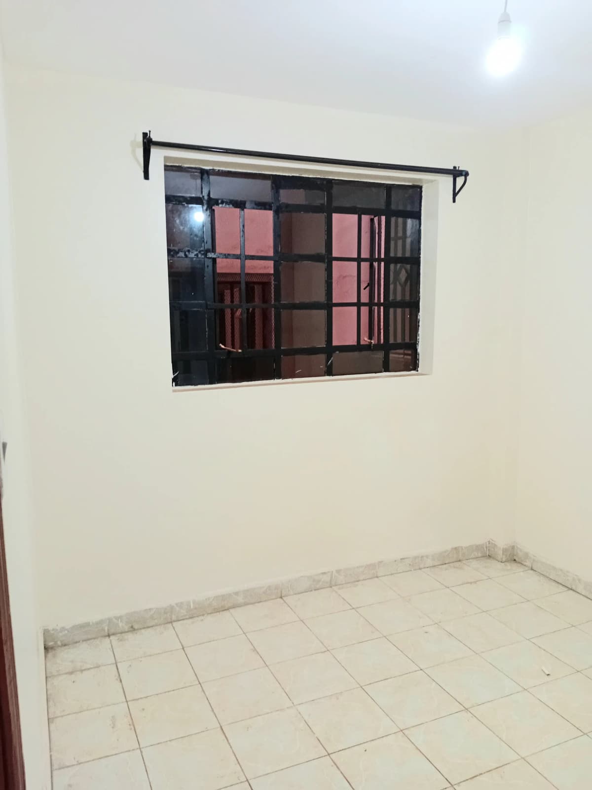 Unfurnished bedroom with barred window and tiled floor
