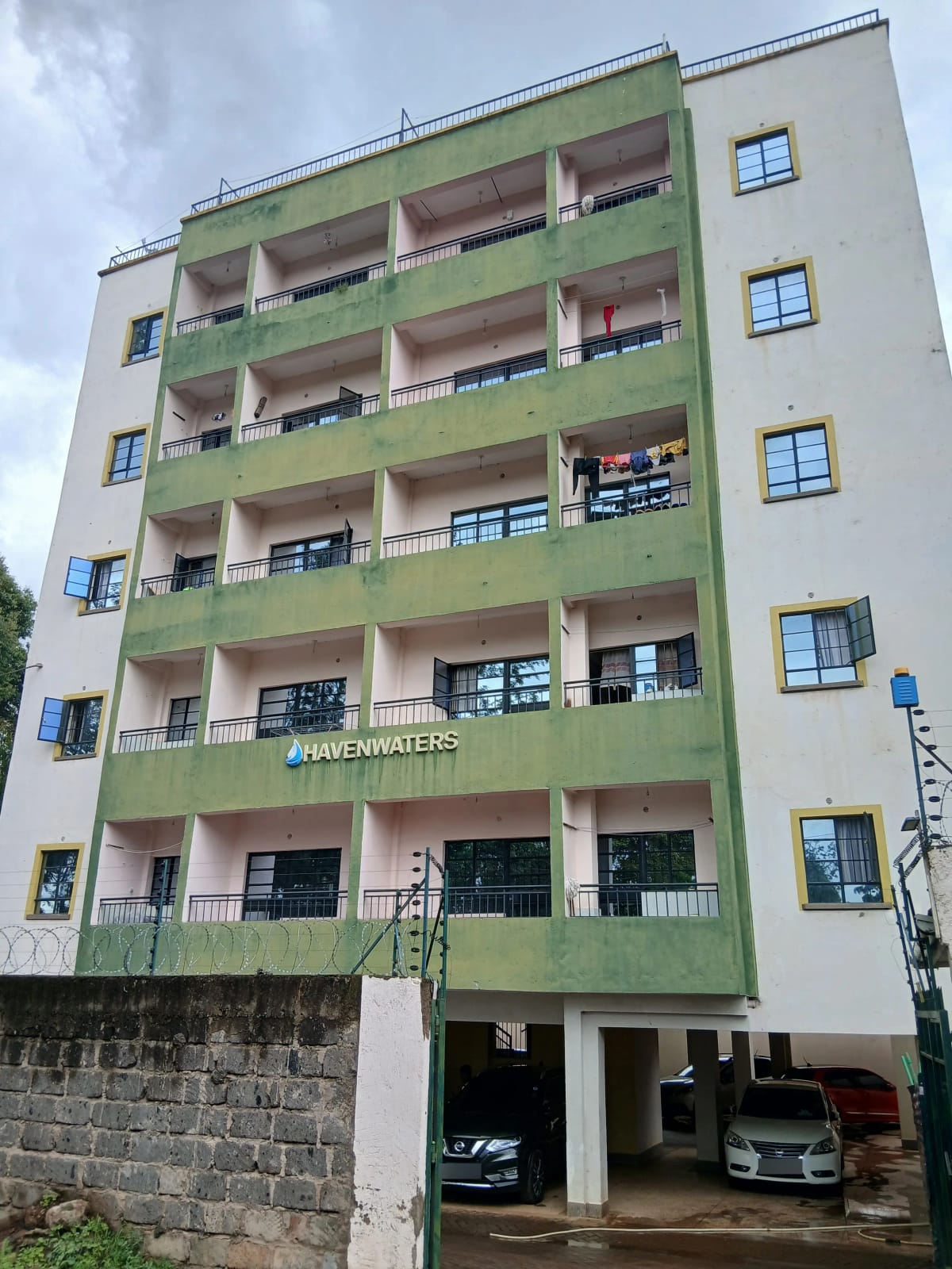 Green multi-story apartment building with ground-floor parking bays