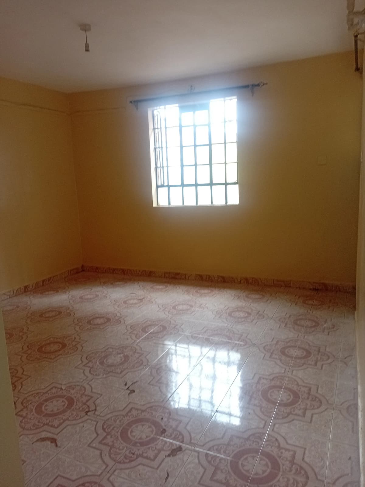 Empty bedroom with patterned tile floor and barred window