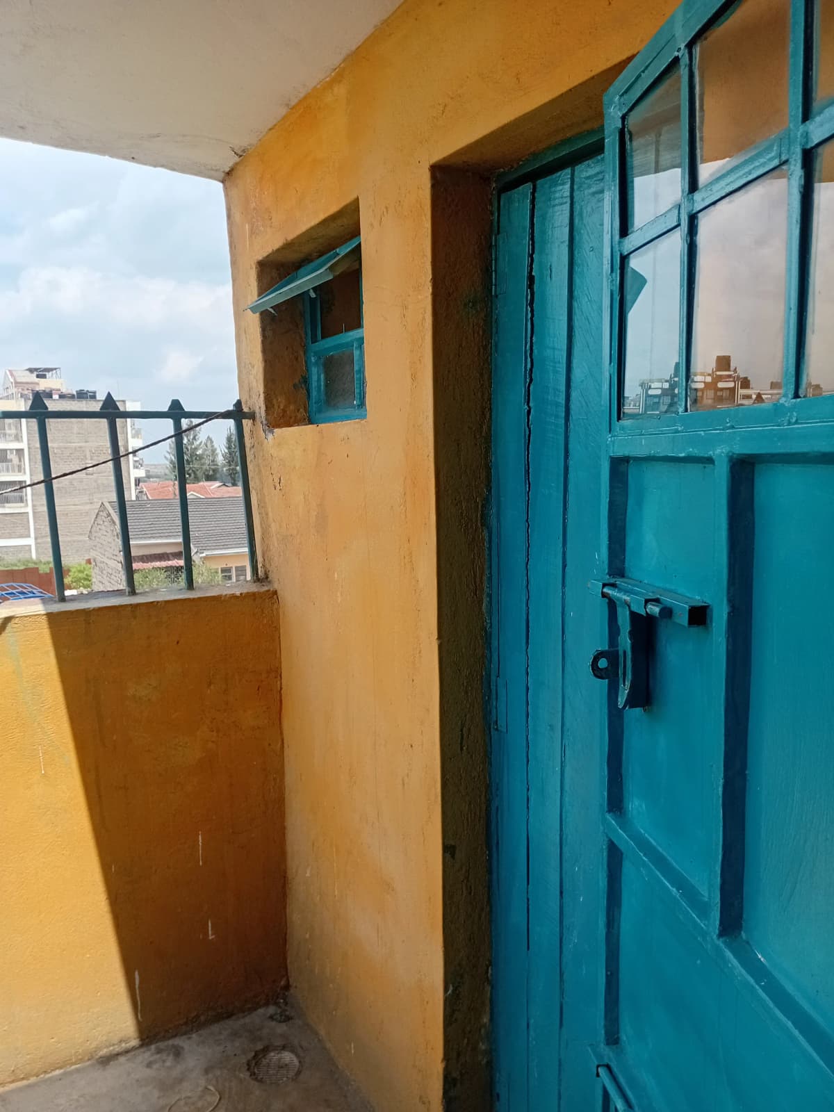 Compact balcony with yellow walls and turquoise door entry