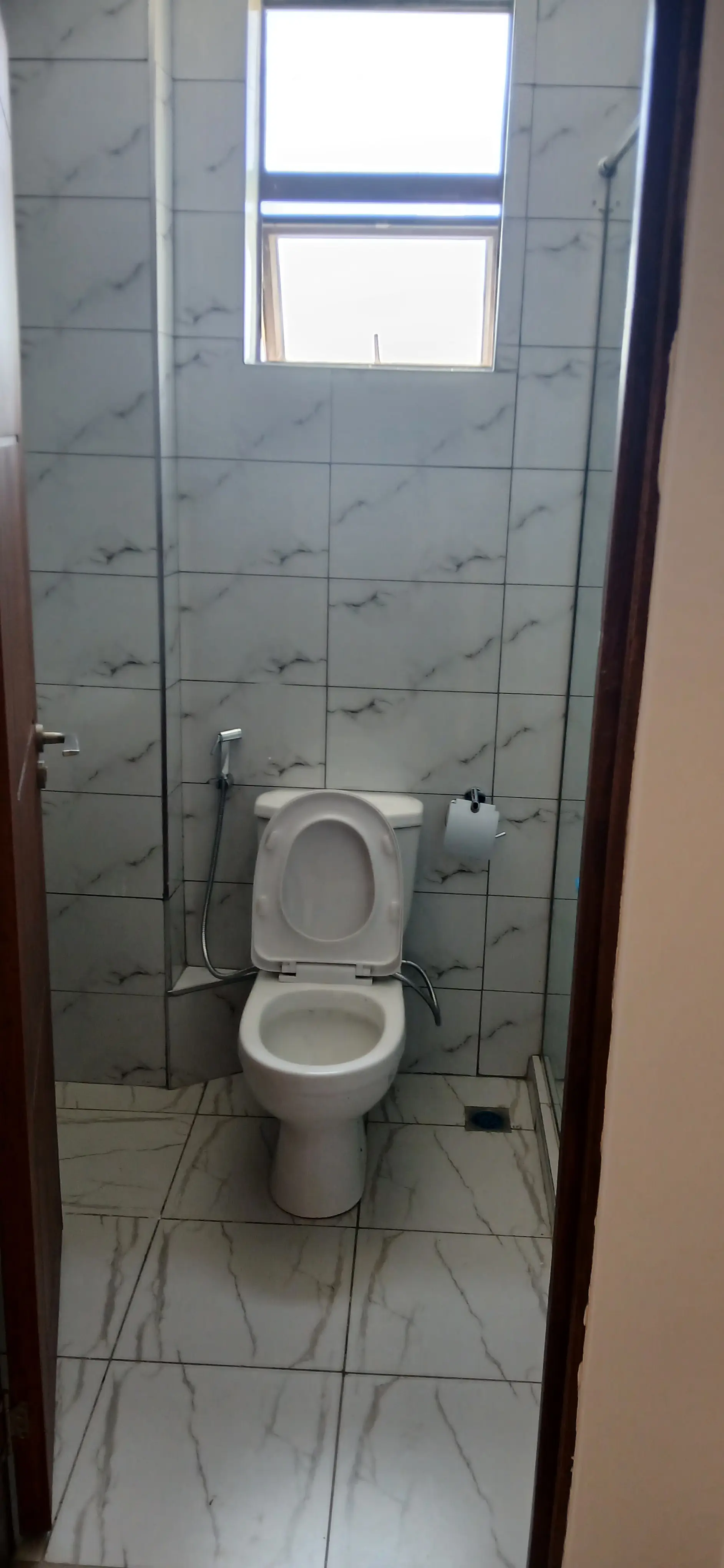Compact bathroom with toilet and window, light tiles
