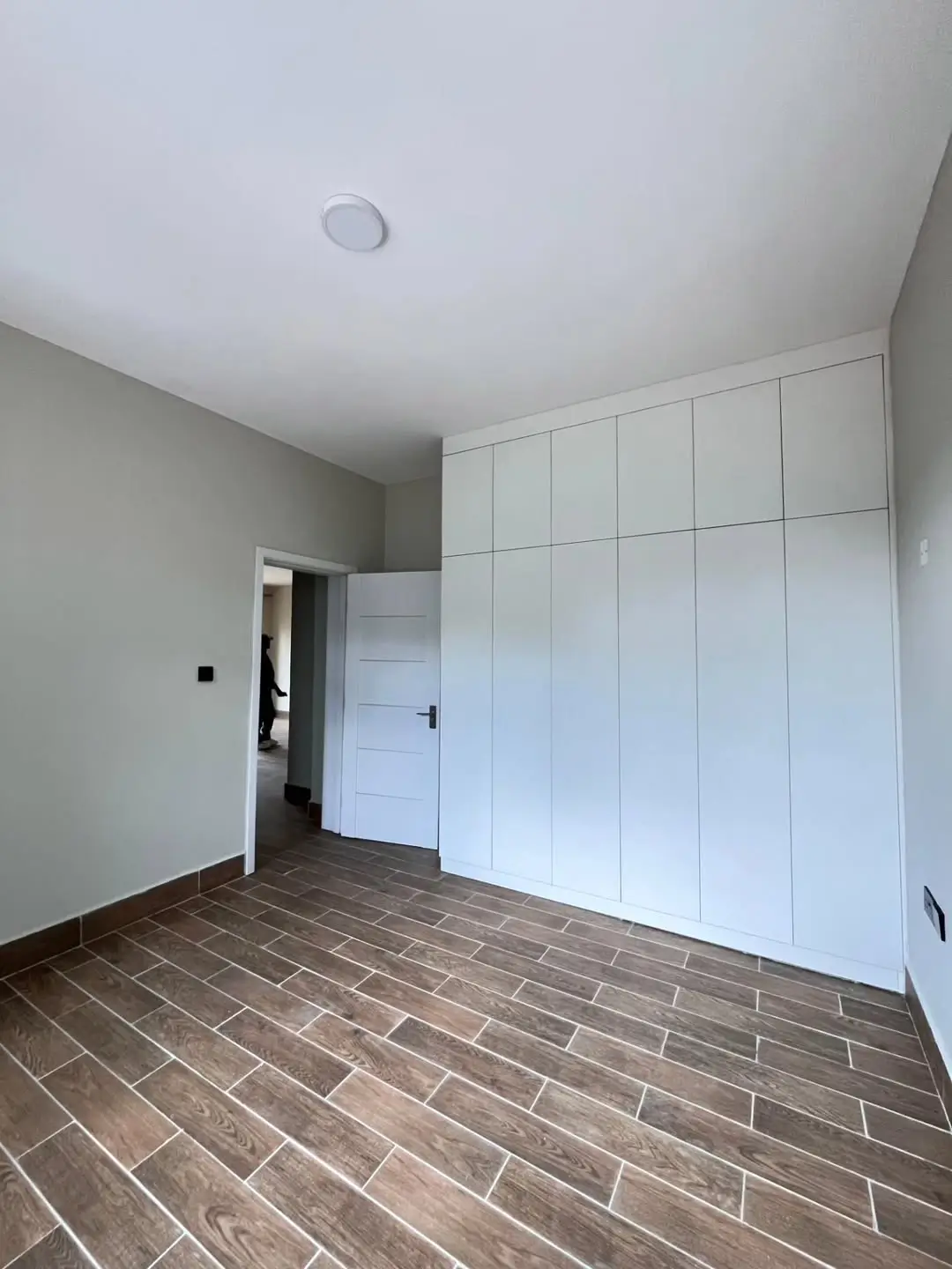 Spacious bedroom with built-in white wardrobes and wood-grain flooring